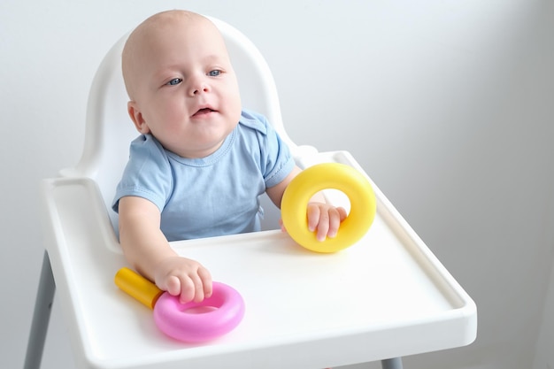 menino bonito brincando com brinquedos de plástico coloridos na cadeira infantil desenvolvimento infantil