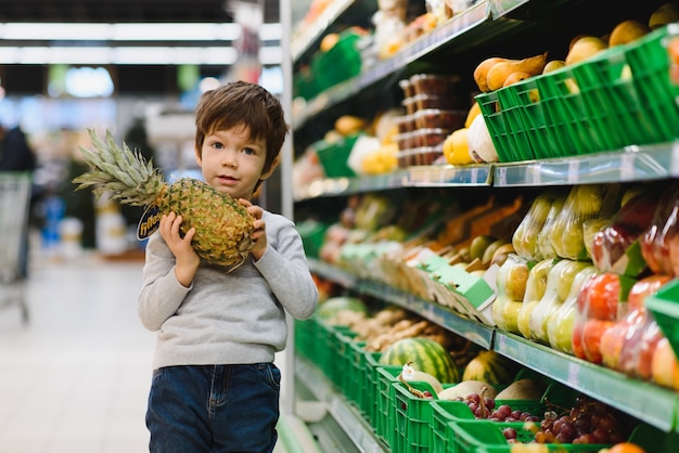 Menino bonito com abacaxi no supermercado