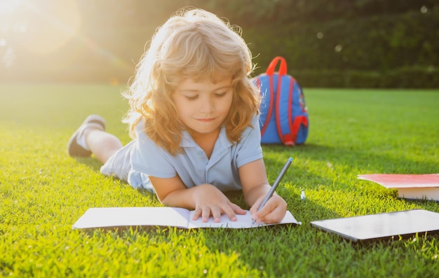 Menino bonito com livros com lápis escrevendo no caderno ao ar livre Acampamento de verão Crianças aprendendo e conceito de educação Dever de casa de férias de verão Estudante pré-escolar ao ar livre