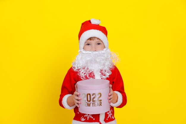 Menino bonito com roupas de Papai Noel e com barba segurando uma caixa de presente redonda rosa nas mãos