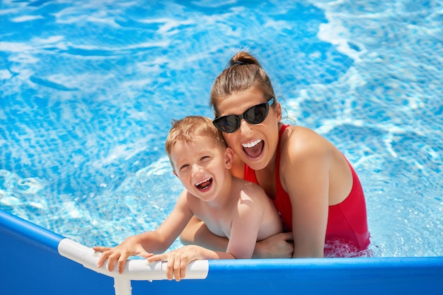 menino bonito com sua mãe brincando em uma piscina de água durante o verão