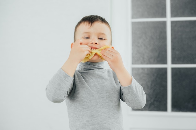 Menino bonito comendo panquecas deliciosas, sentado a uma mesa sobre um fundo claro