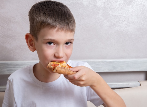 Menino bonito, comendo uma fatia de pizza de calabresa e queijo, close-up, copie o espaço. Conceito de alimentos pouco saudáveis, comida favorita das crianças.