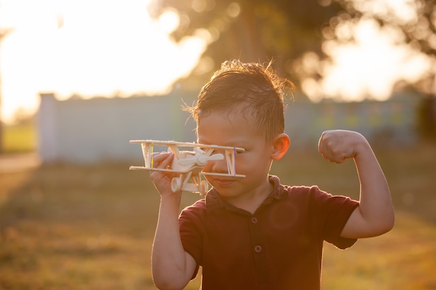 Foto menino bonito criança asiática brincando com o avião de madeira de brinquedo no parque na hora por do sol com diversão