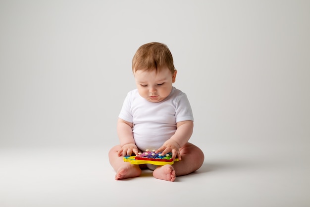 Menino bonito da criança 8 meses de idade em bodysuit branco brinca com o desenvolvimento de sessão de brinquedo