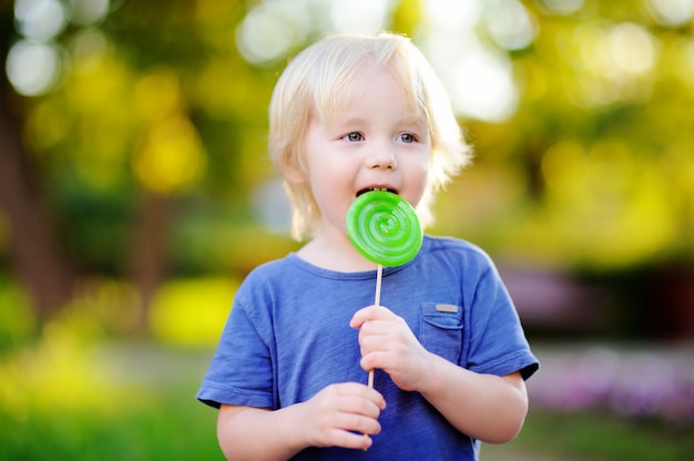 Menino bonito da criança com o pirulito verde grande. Criança comendo doce barra de chocolate. Doces para crianças e jovens. Diversão ao ar livre de verão