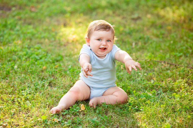 Menino bonito da criança em body azul, sentado na grama