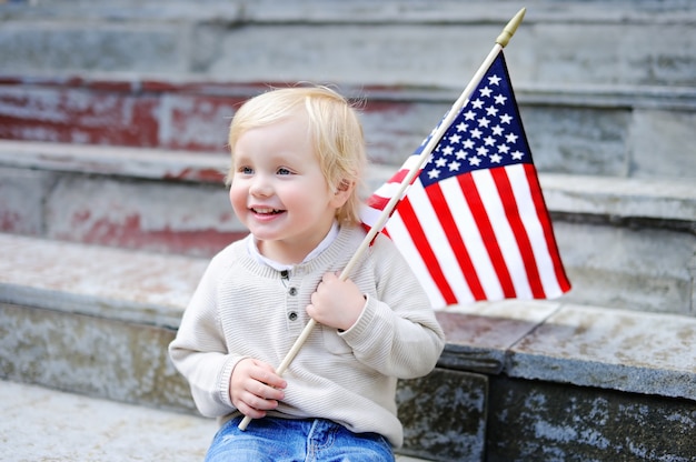 Menino bonito da criança que guarda a bandeira americana. Conceito do dia da independência.