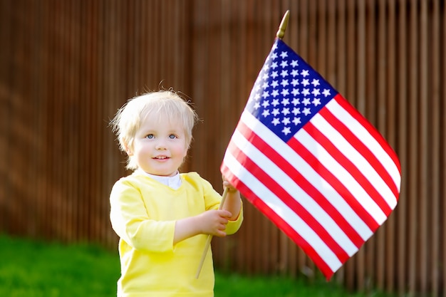 Menino bonito da criança que guarda a bandeira americana.