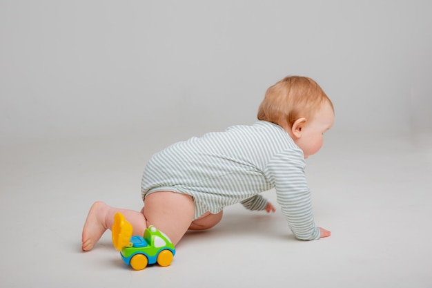 Menino bonito da criança velho em roupa branca brinca com brinquedo de carro sentado em um espaço de fundo branco para te