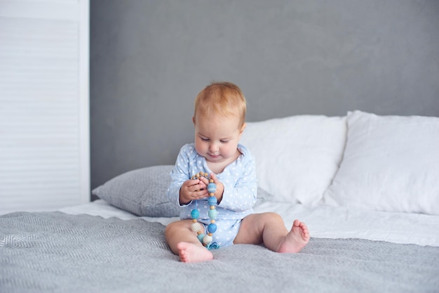 Menino bonito de 8 meses brincando com brinquedo de malha na cama em casa