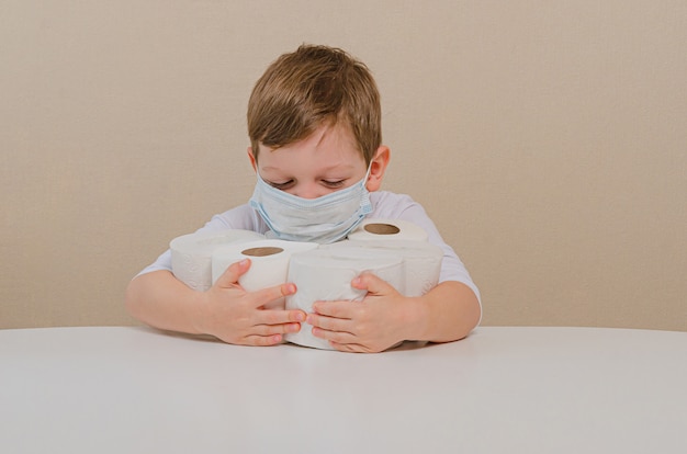 Menino bonito de quatro em uma máscara médica protetora brinca com papel higiênico