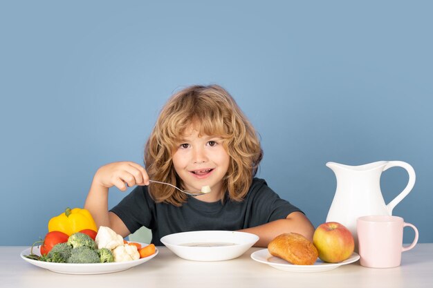 Menino bonito e feliz tomando sopa no almoço garoto comendo sopa criança comendo comida saudável no estúdio iosol