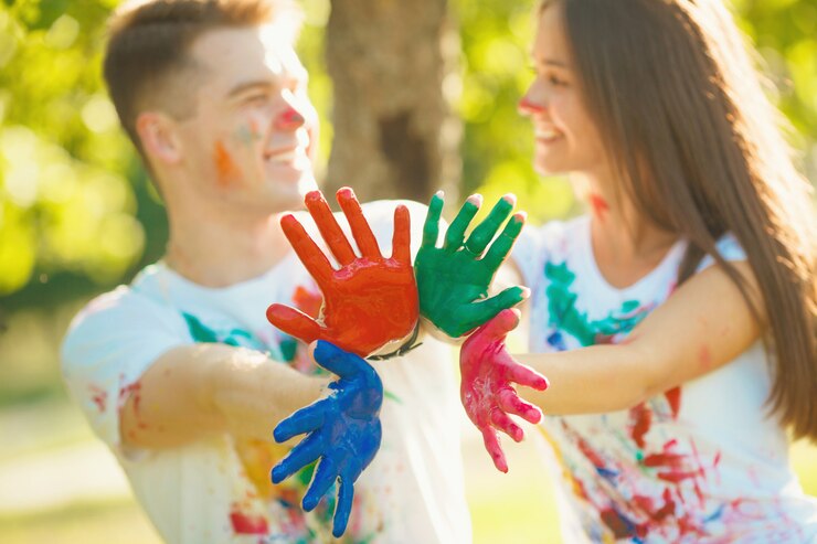 Menino bonito e menina que agitam suas mãos ou palmes pintadas na câmera e no sorriso. Na frente da câmera em foco, há um plano multicolorido das mãos do casal apaixonado.