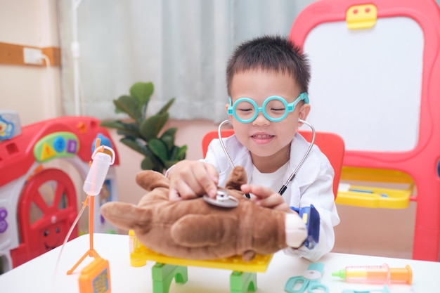 Menino bonito e sorridente asiático de 3 a 4 anos em uniforme de médico se divertindo brincando de médico