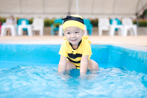 Foto menino bonito em maiô amarelo jogar na bela piscina azul