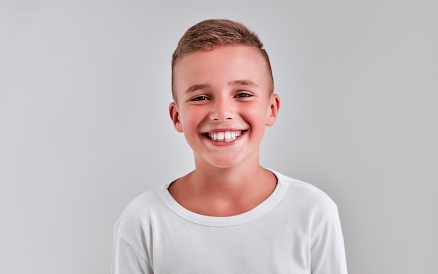 Foto menino bonito em um fundo cinza com uma jaqueta branca sorrindo