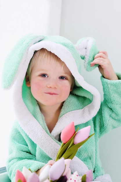 Menino bonito em uma fantasia de coelho com um buquê de flores no dia das mães.