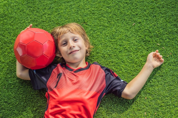 Menino bonito em uniforme vermelho jogando futebol no campo ao ar livre Criança ativa fazendo esportes com crianças ou pai Rindo menino feliz se divertindo no verão