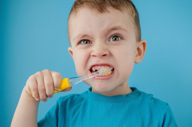 Menino bonito, escovando os dentes na parede azul