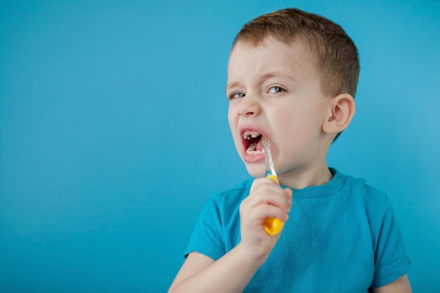 Menino bonito, escovando os dentes no fundo azul