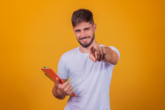 Menino bonito jovem estudante segurando livros sobre fundo amarelo.