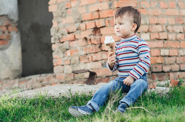 Foto menino bonito menino menino de três anos comendo sorvete muito apetitoso em fundo de parede de tijolos