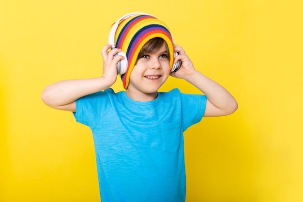 Menino bonito na camisa azul e chapéu colorido com fundo amarelo de fones de ouvido