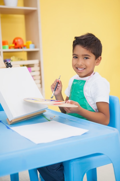 Menino bonito pintando na mesa na sala de aula