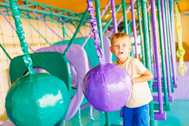Menino bonito rastejando e brincando em um playground colorido em um parque de diversões coberto