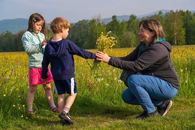 Menino bonito segurando e dando um buquê de flores silvestres Crianças um menino e uma menina coletaram flores no prado para sua mãe conceito de dia das mães Crianças na natureza