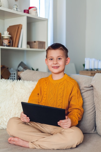 Menino bonito usa um tablet. O menino fala por link de vídeo. Quarentena. Casa.