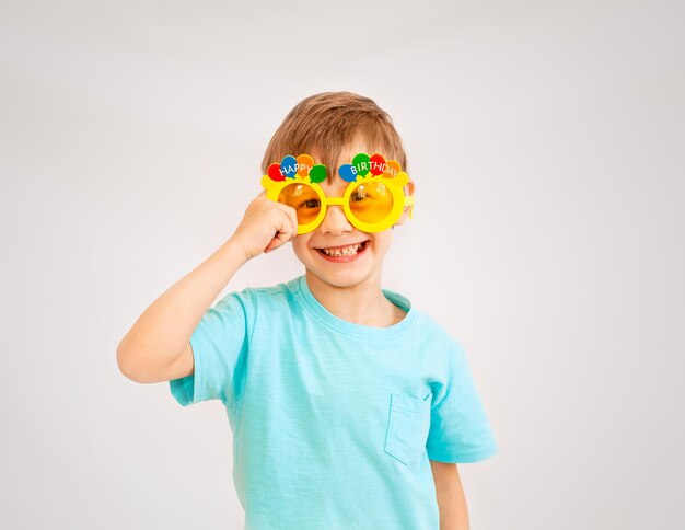 Menino bonito usando óculos de festa com texto de feliz aniversário. menino de óculos amarelos