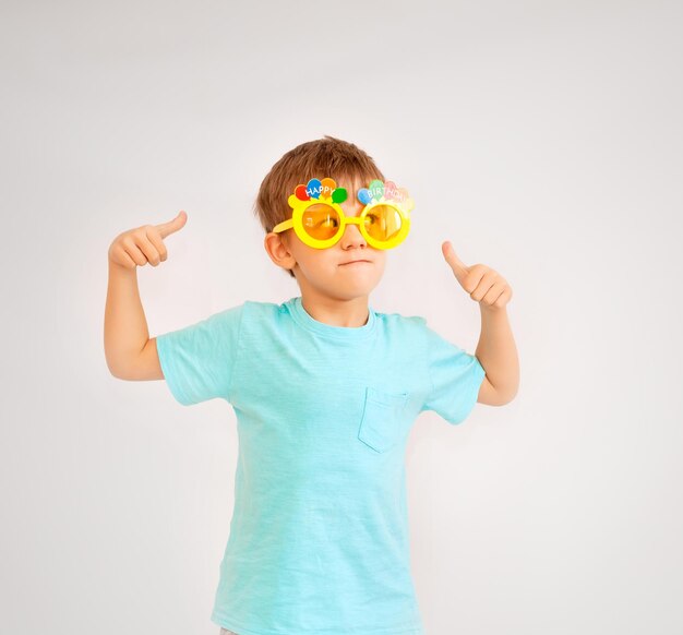 Menino bonito usando óculos de festa com texto de feliz aniversário. menino de óculos amarelos