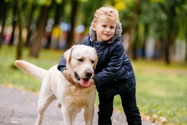 Menino brinca, corre com seu cachorro Labrador no parque no outono