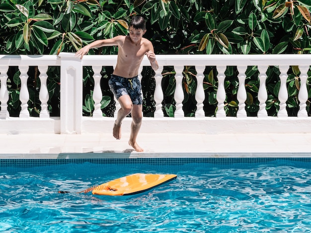 Foto menino brinca na piscina pulando em uma pequena prancha de surfe para manter o equilíbrio