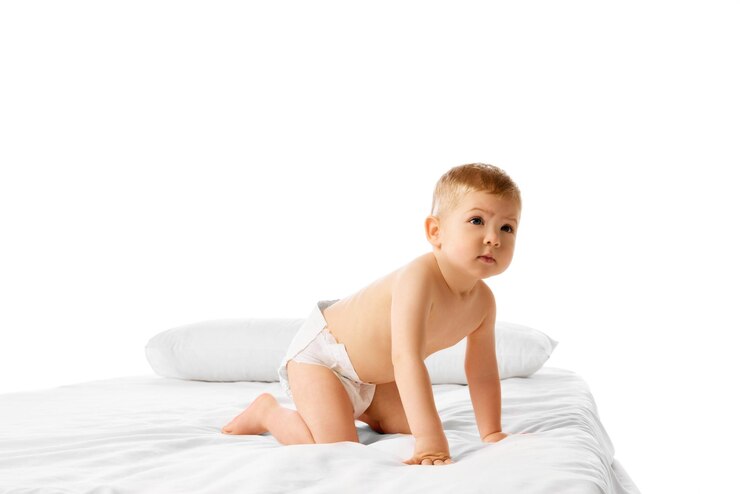 Foto menino brincalhão em fraldas de pé na cama isolado sobre fundo branco do estúdio