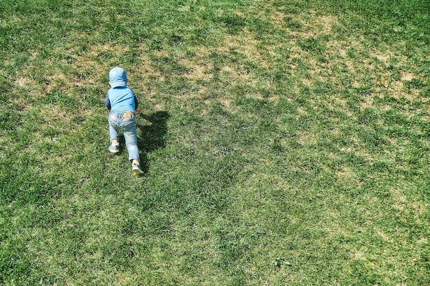 Menino brincalhão sobe a encosta íngreme da colina coberta com grama verde exuberante na vista traseira do parque