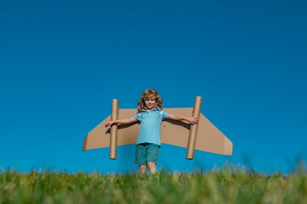 Menino brincando com asas de avião de brinquedo de papelão no céu com espaço de cópia para texto criativo w