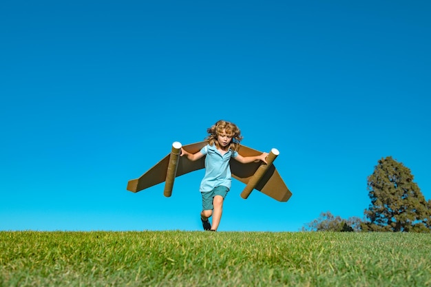 Menino brincando com asas de avião de brinquedo de papelão no céu com espaço de cópia para texto criativo w