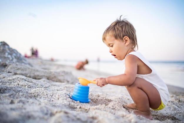 Menino brincando com brinquedos na praia construindo contas e torres sorrindo para alguém nos bastidores nas férias de verão