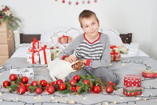 menino brincando com cachorro jack russell em uma cama com decoração de ano novo