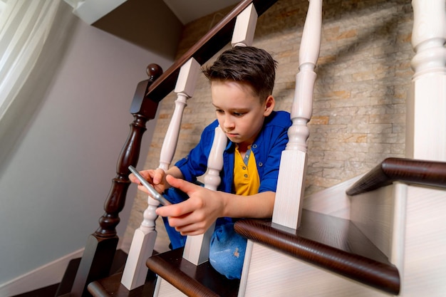 Menino brincando com smartphone sentado na escada Vista de cima