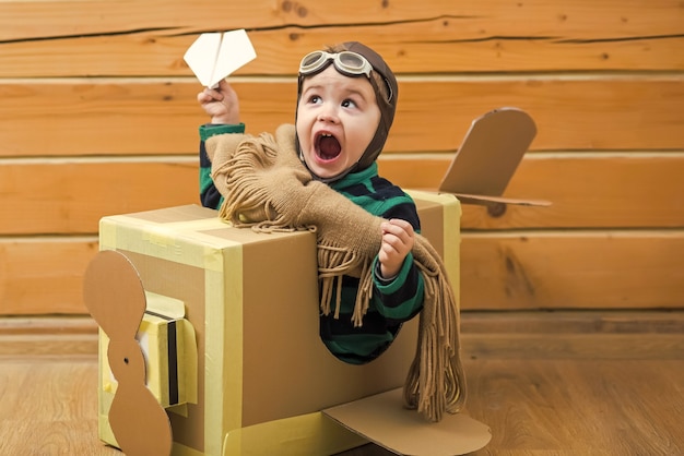 Menino brincando com um avião de papelão na sala de madeira