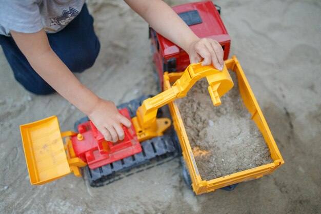 Menino brincando com um carro de brinquedo em uma areia Criança construindo areia no quintal