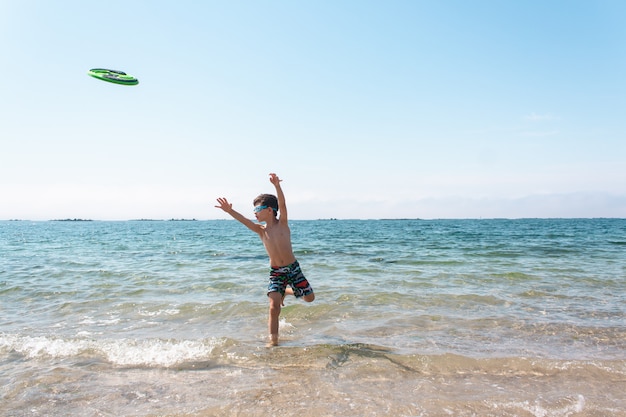 Menino brincando com um disco de frisbee na praia