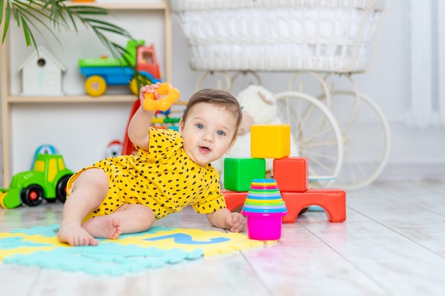 Menino brincando no quarto das crianças em um macacão amarelo com brinquedos coloridos brilhantes