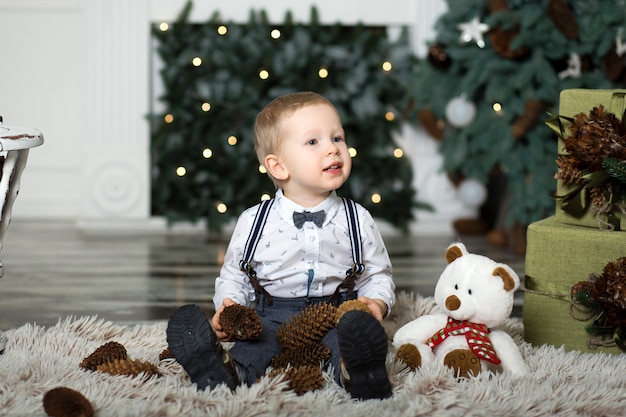 Menino brincar com pinhas perto de uma árvore de natal.