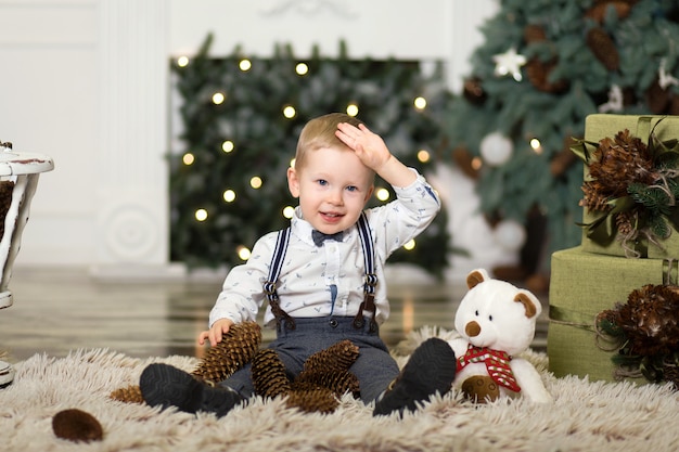 Menino brincar com pinhas perto de uma árvore de natal.