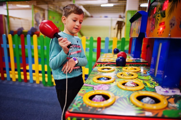 Foto menino brincar em acertar a máquina de jogo de hamster no playground coberto.